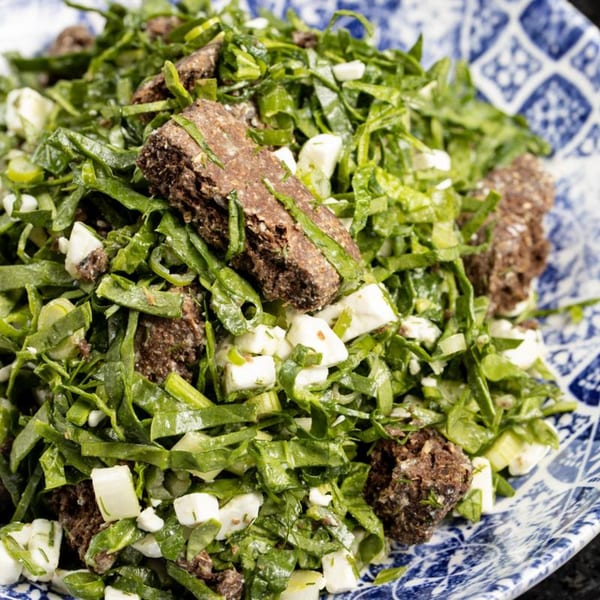 Close-up of a Greek salad with greens, feta, and meat on a blue and white patterned plate.