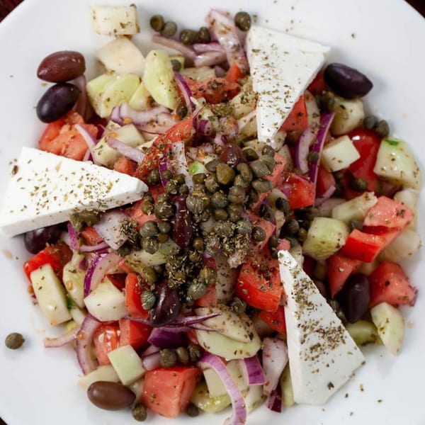 Close-up of a Greek salad with feta, tomatoes, cucumbers, red onions, olives, and capers.