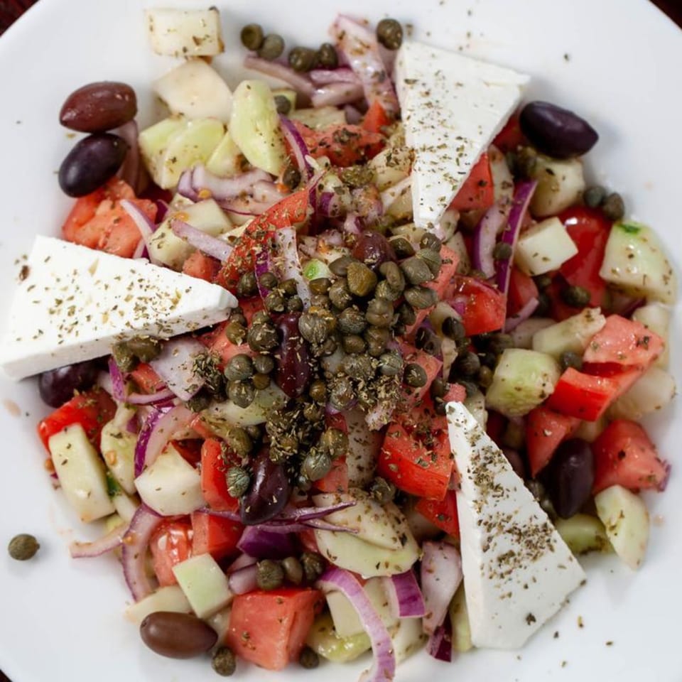 Close-up of a Greek salad with feta, tomatoes, cucumbers, red onions, olives, and capers.
