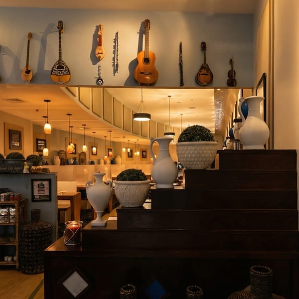 A restaurant interior with traditional Greek instruments on the wall and decorative vases on a dark wooden staircase.