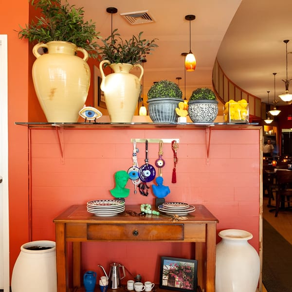 A vibrant restaurant interior with orange walls, decorative vases, evil eye charms, and a wooden console table.