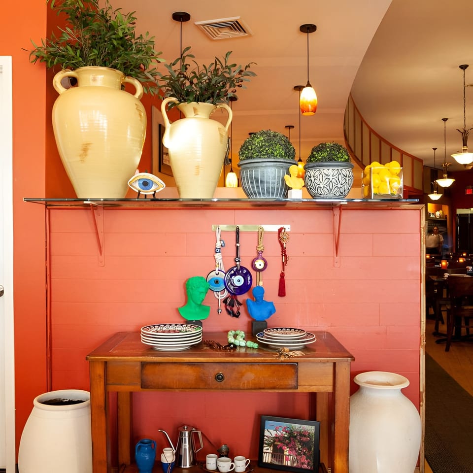 A vibrant restaurant interior with orange walls, decorative vases, evil eye charms, and a wooden console table.