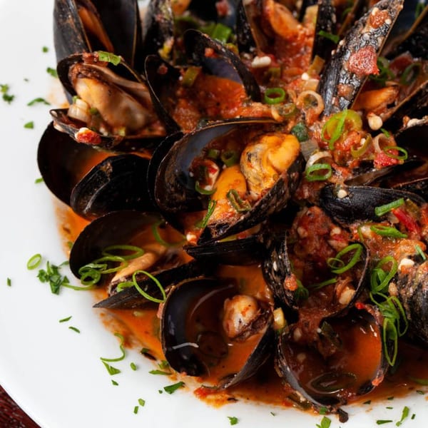 Steamed mussels in a rich red sauce, garnished with green onions and parsley.