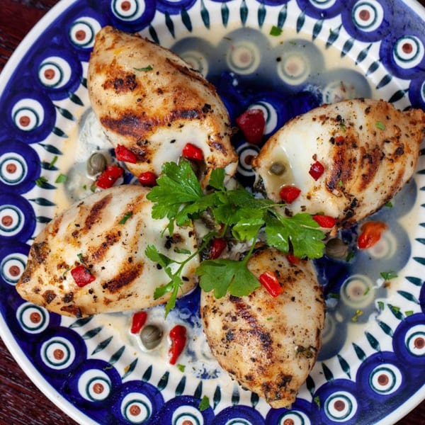 Grilled calamari with red peppers, capers, and parsley on a blue and white Greek plate.