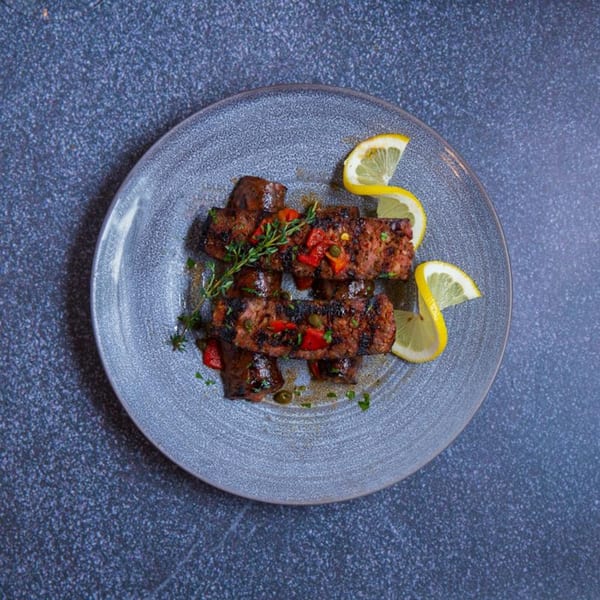 Grilled meat skewers with red peppers, herbs, and lemon slices on a gray plate.