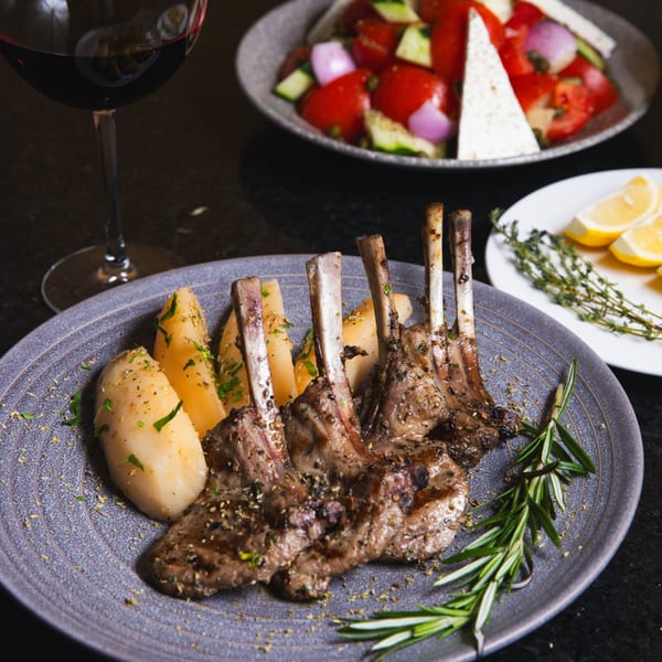 Grilled lamb chops with roasted potatoes and rosemary, served with a Greek salad and red wine.
