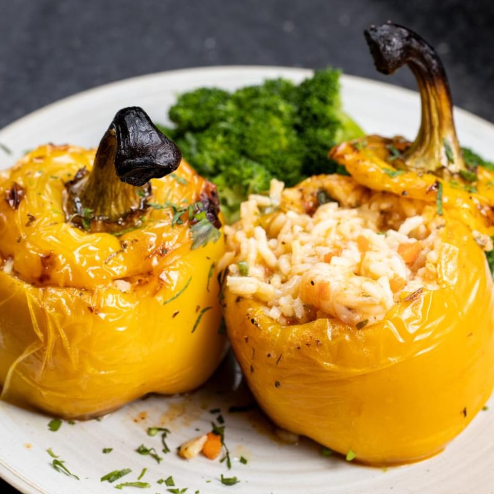 Two yellow stuffed bell peppers with rice and herbs, served with broccoli on a white plate.