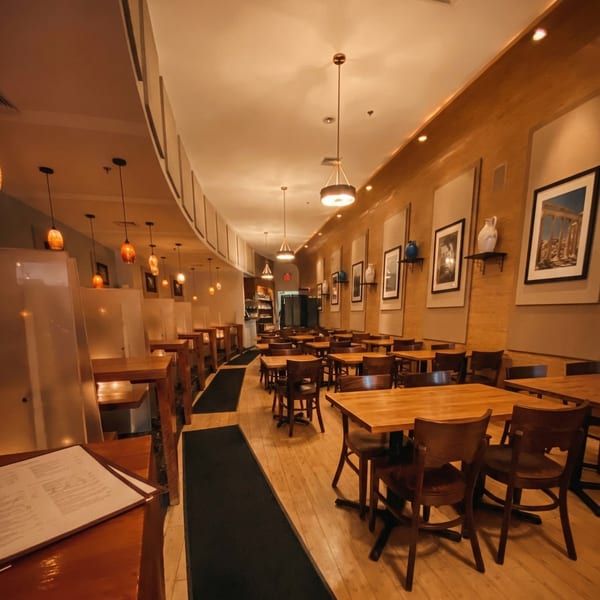 Empty restaurant dining room with wooden tables, chairs, and warm lighting, featuring framed art on the walls.