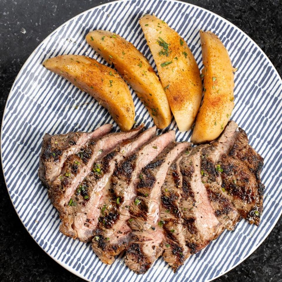 Grilled steak slices and seasoned potato wedges on a blue and white striped plate.