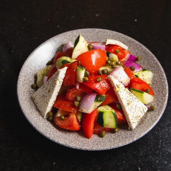 A vibrant Greek salad with tomatoes, cucumbers, red onions, capers, and feta cheese.