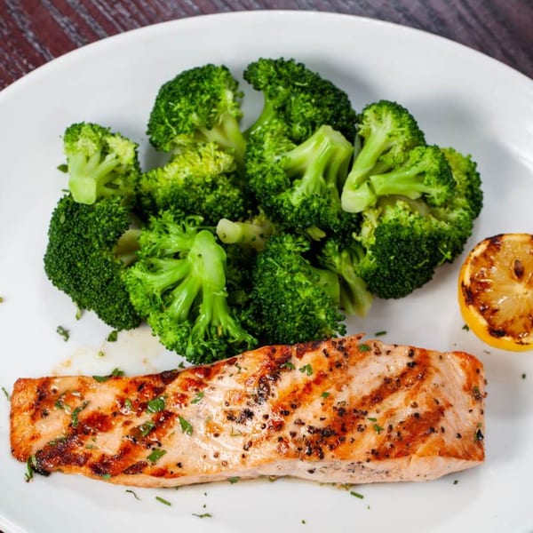 Grilled salmon fillet with broccoli and a charred lemon half on a white plate.
