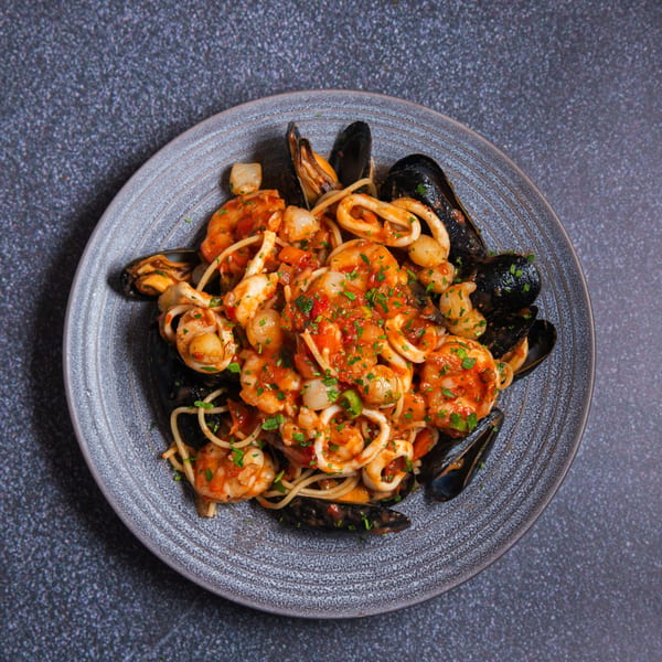 Seafood pasta with mussels, shrimp, scallops, and calamari in a rich red sauce, garnished with parsley.