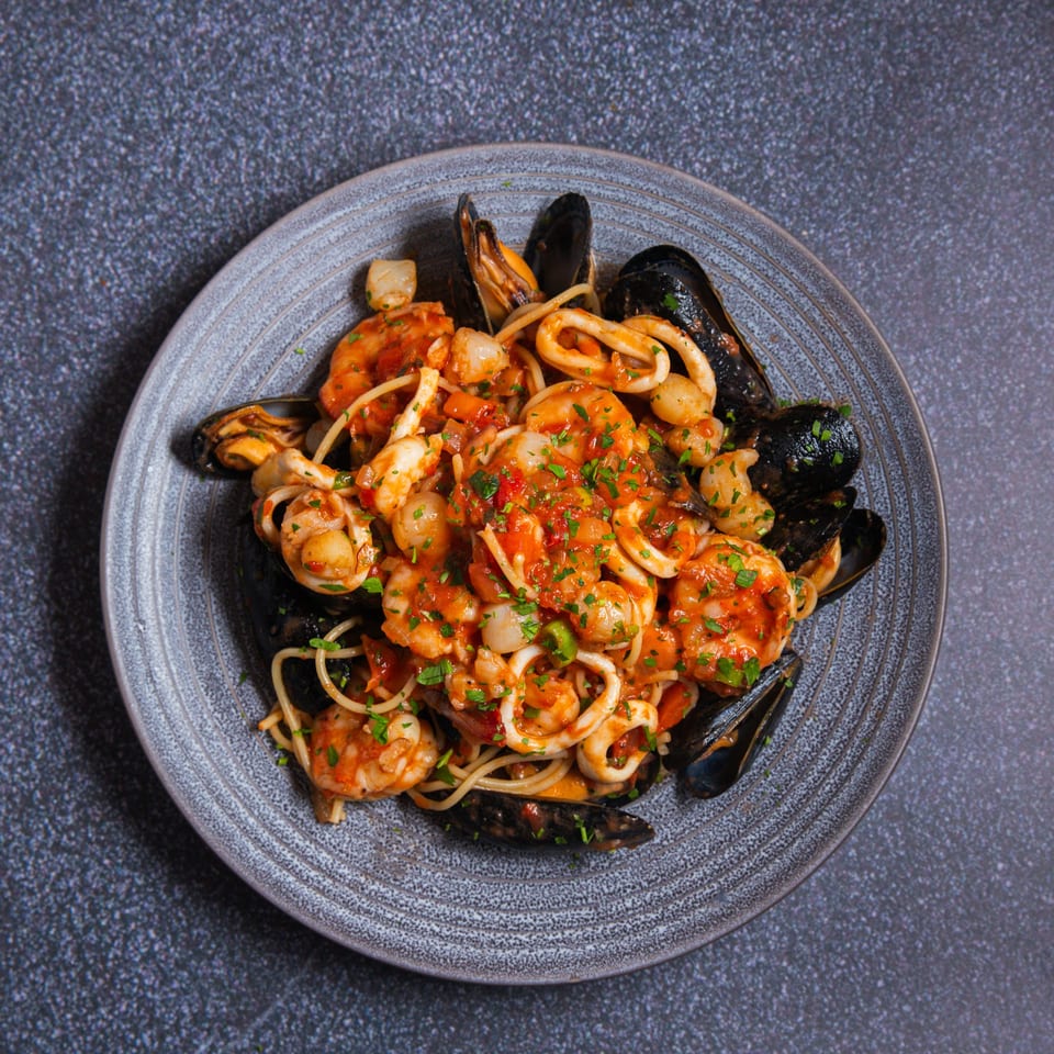 Seafood pasta with mussels, shrimp, scallops, and calamari in a rich red sauce, garnished with parsley.