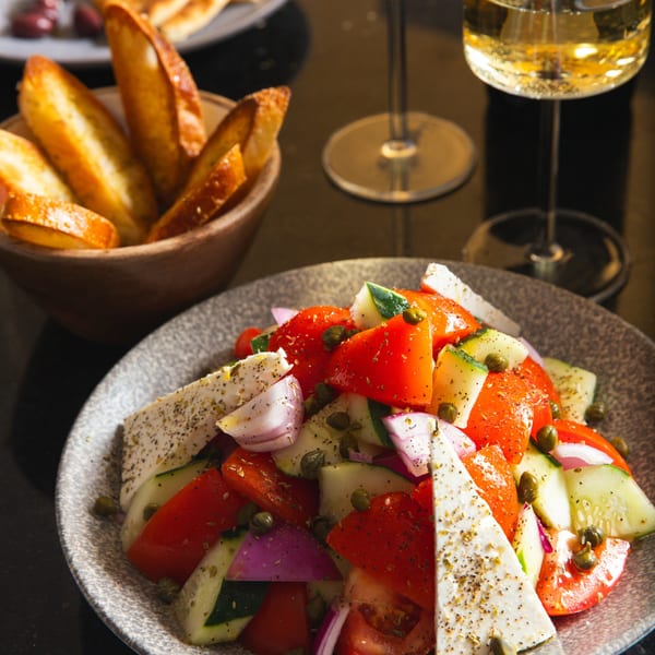 Greek salad with feta, tomatoes, cucumbers, onions, capers, and a side of toasted bread.