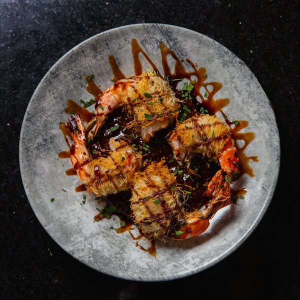 Four crispy shrimp with dark sauce and green herbs on a gray plate.