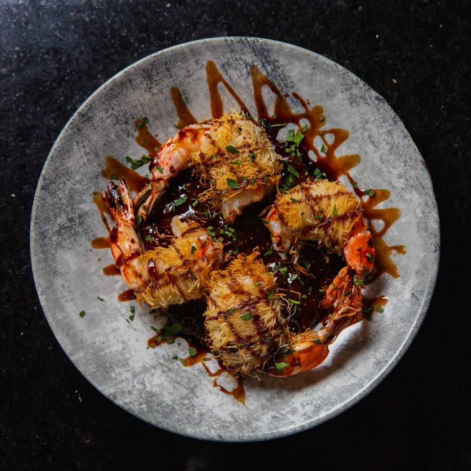 Four crispy shrimp with dark sauce and green herbs on a gray plate.