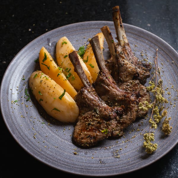 Grilled lamb chops with bone, seasoned potatoes, and dried herbs on a gray plate.