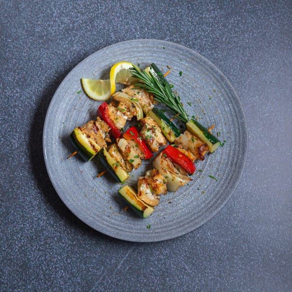 Grilled chicken and vegetable skewers with lemon and rosemary on a gray plate.